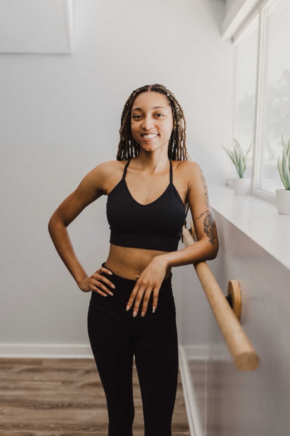 Amaya Johnson smiling in a movement studio, one hand on her hip, leaning on a ballet barre